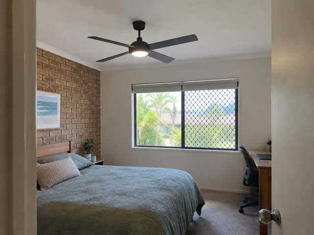 Bedroom with a black ceiling fan, brick feature wall and window in Robina